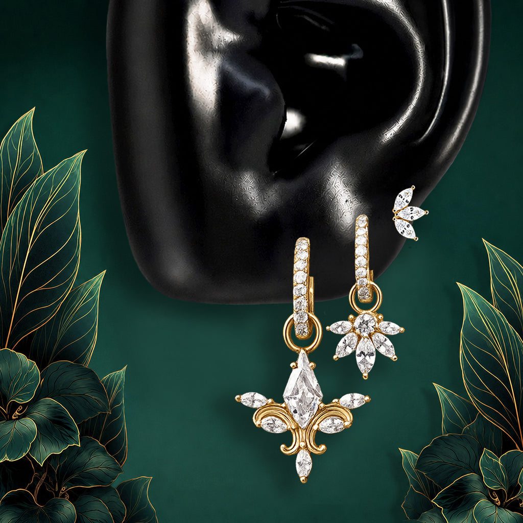 IMBER Otherworldly gold bridal earring stack with pavé huggies, an ornate fleur-de-lis crystal drop, a floral charm, and a marquise leaf stud for a statement ear stack